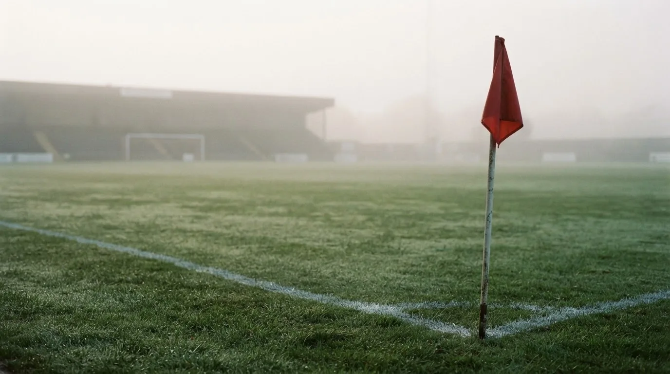 Der Rand eines Spielfelds mit weißer Linie und Eckfahne bei Nebel am frühen Morgen, ohne Menschen.
