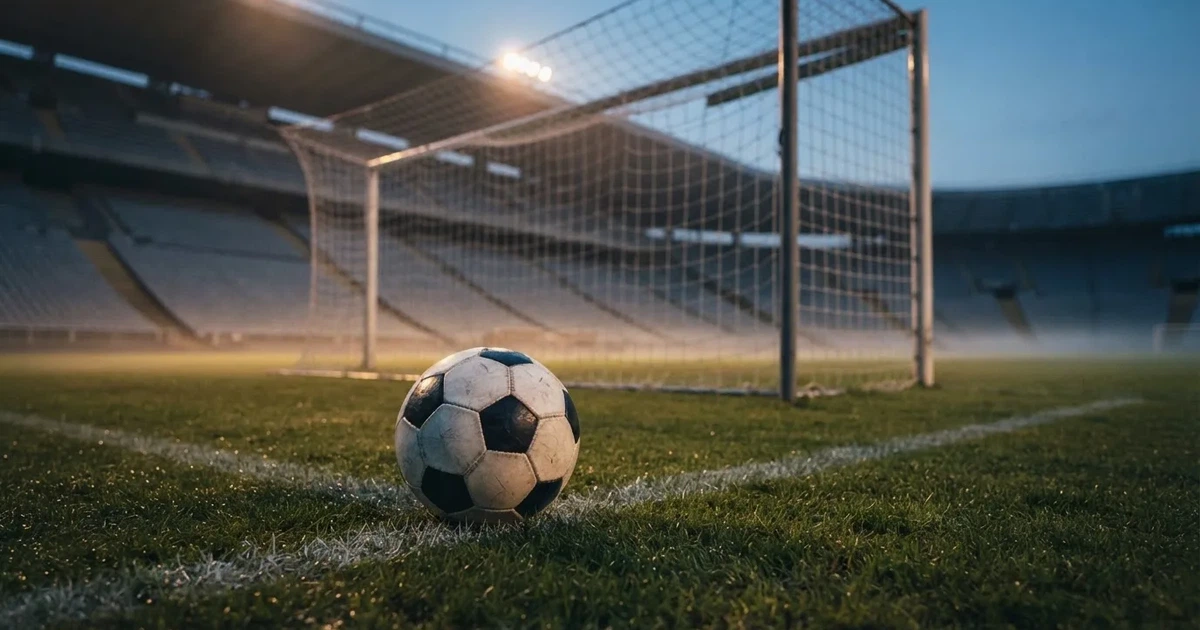 Ein Fußball liegt im Strafraum direkt vor dem Tor mit Netz, im Hintergrund leere Ränge bei Dämmerung.