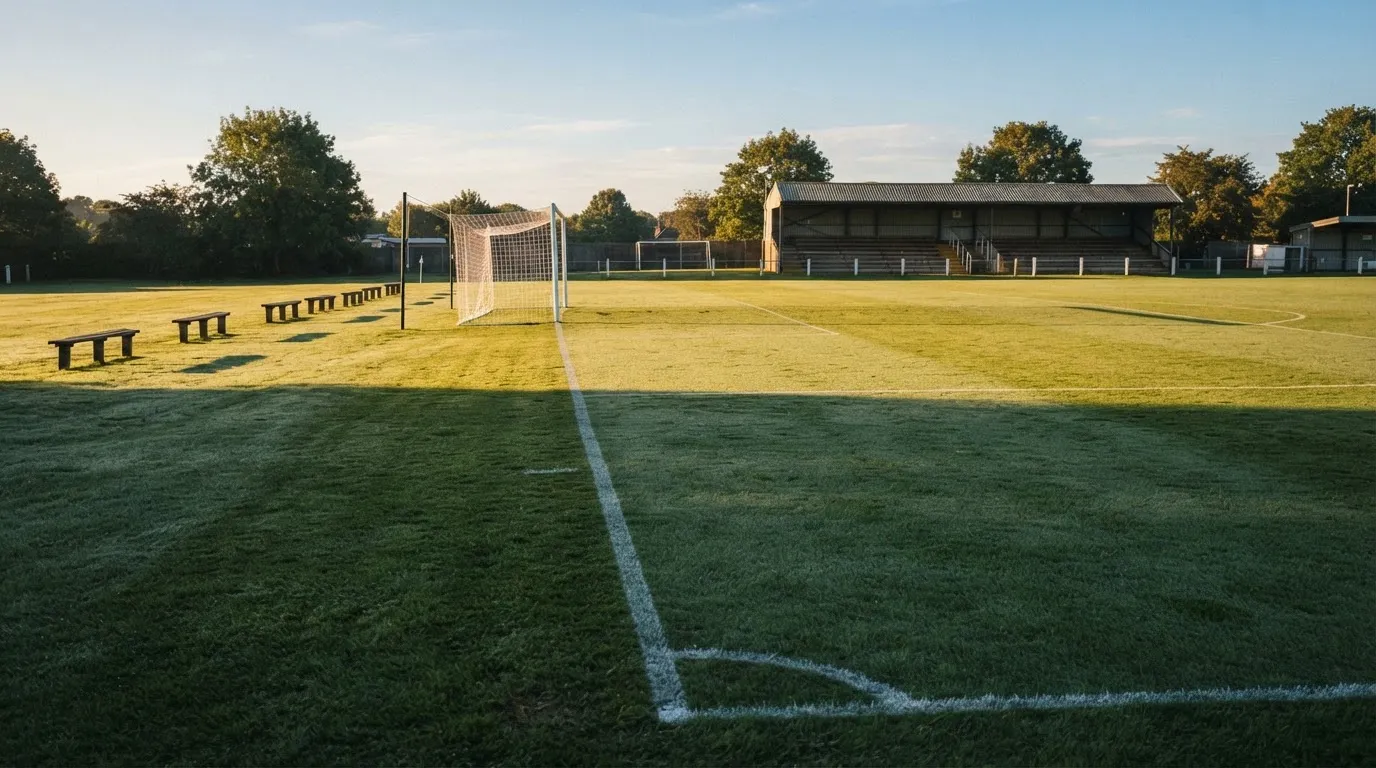 Ein Fußballplatz mit frisch gezogenen Kreidelinien im ersten Morgenlicht, leere Ersatzbänke am Spielfeldrand.