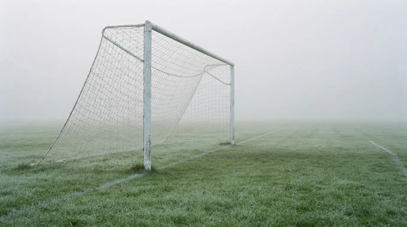 Ein Fußballtor mit Netz im Morgennebel auf einem leeren Platz, die Linien nur schwach zu erkennen.