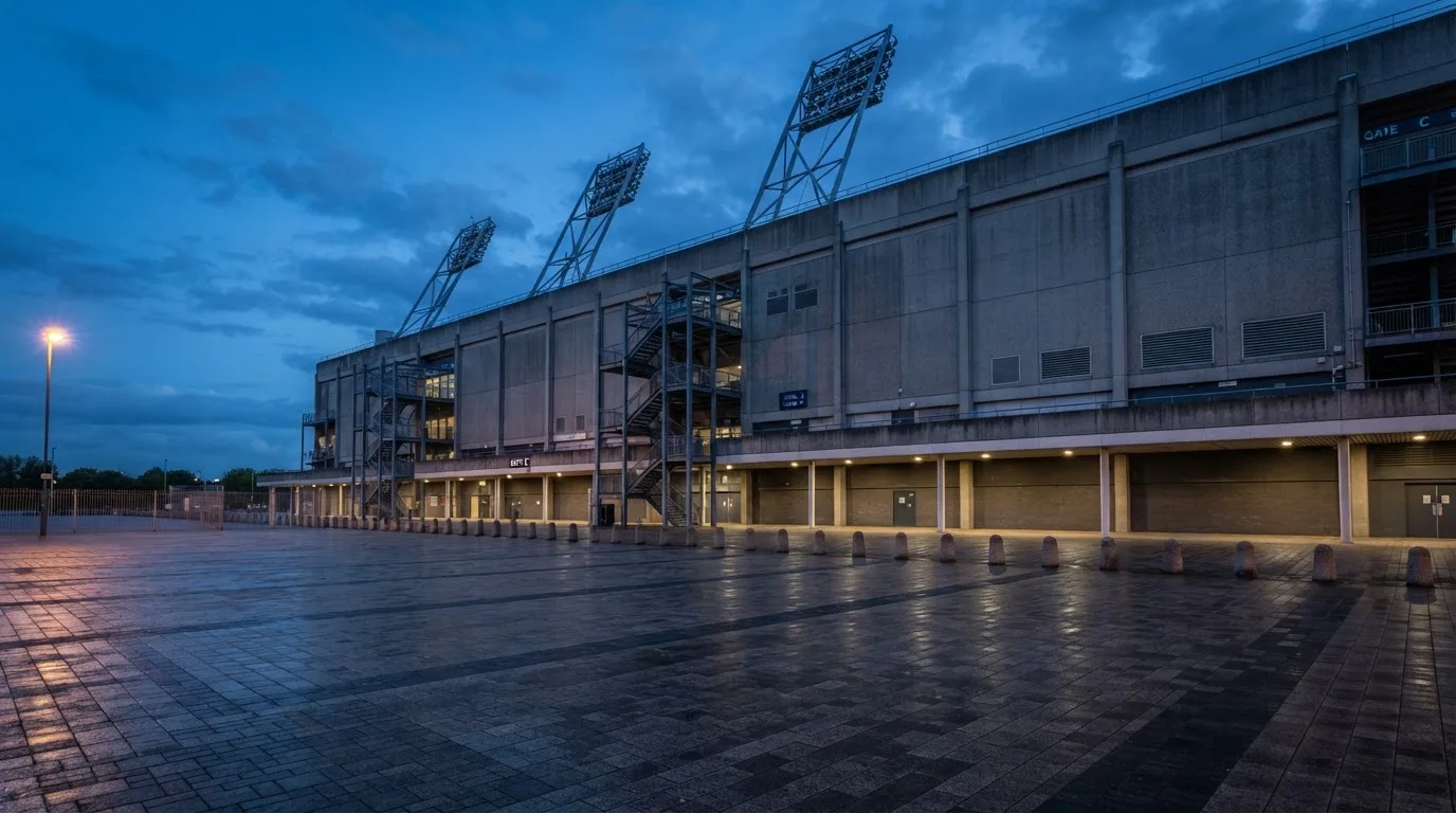 Die Rückseite einer Tribüne bei Dämmerung, davor ein menschenleerer Vorplatz mit Pflastersteinen.