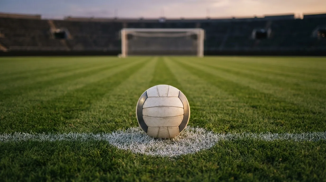 Ein Fußball liegt auf dem Elfmeterpunkt eines leeren Platzes im Abendlicht.