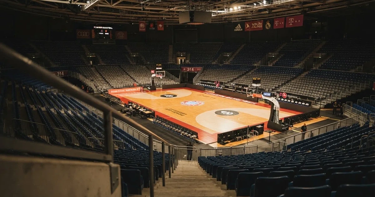 Eine leere Basketballhalle von einer oberen Tribünenreihe aus gesehen, Parkett und Körbe im Licht der Hallenstrahler.