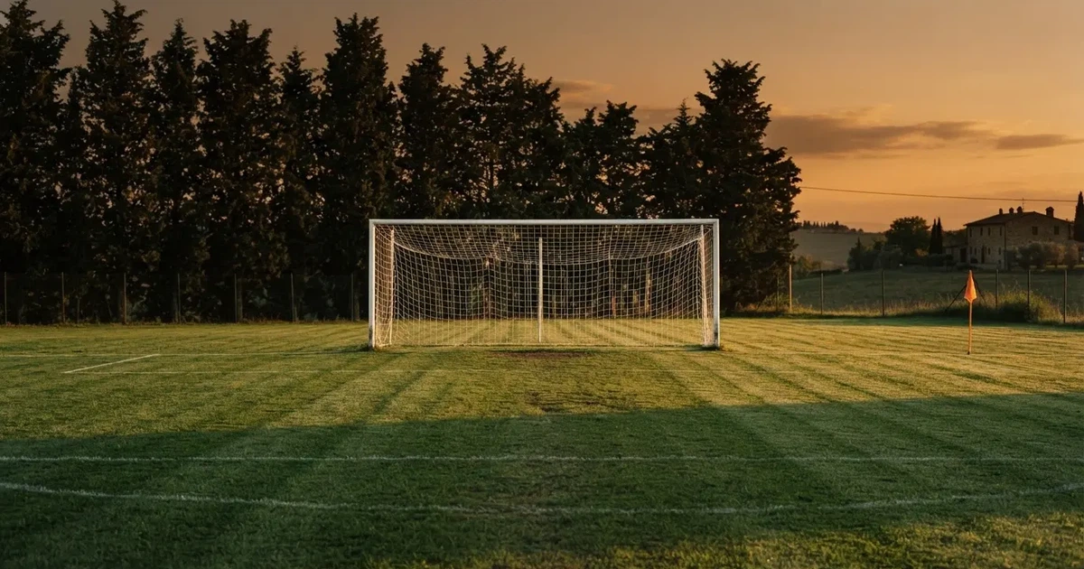 Ein Fußballtor mit Netz auf einem leeren Platz im Abendlicht, der Rasen frisch gemäht, im Hintergrund Zypressen.