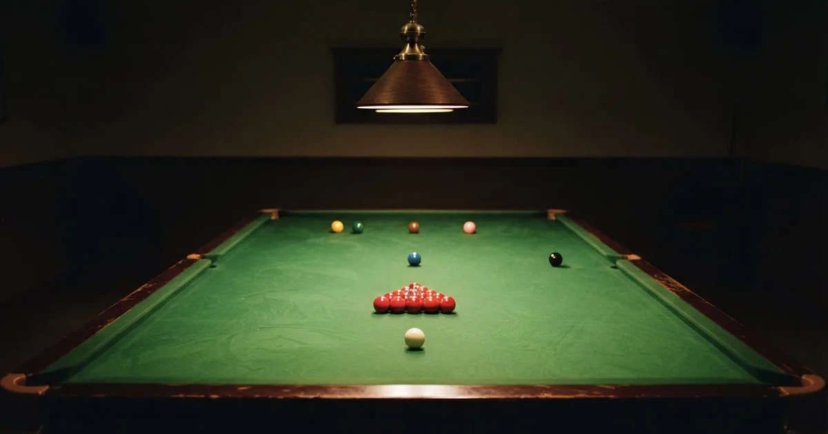Ein Snookertisch mit grünem Tuch und aufgebauten roten Kugeln in einem abgedunkelten Raum unter einer hängenden Lampe.
